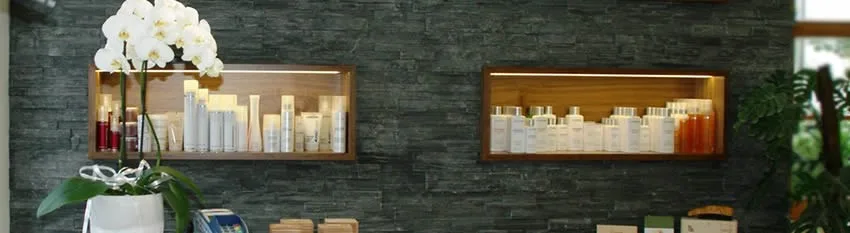 Produktregale und dunkle Steinwand im Salon von Hair Design Metzler